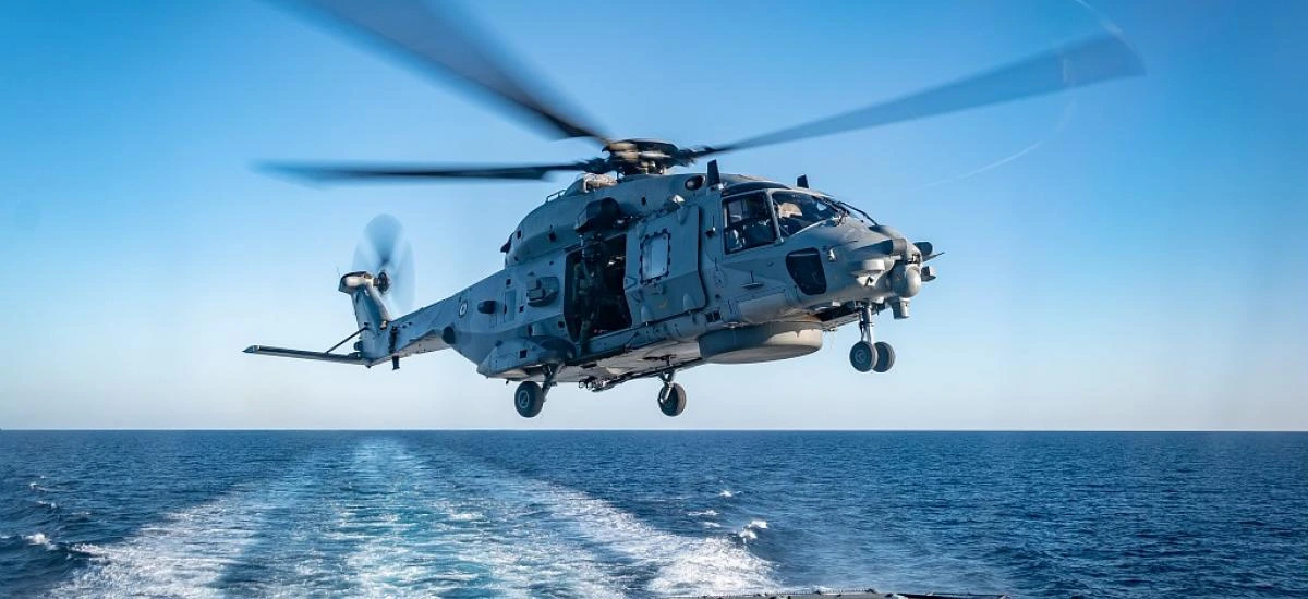 Un hélicoptère Caïman de la Marine nationale en vol stationnaire au-dessus de la mer, dans le sillage d'un bâtiment