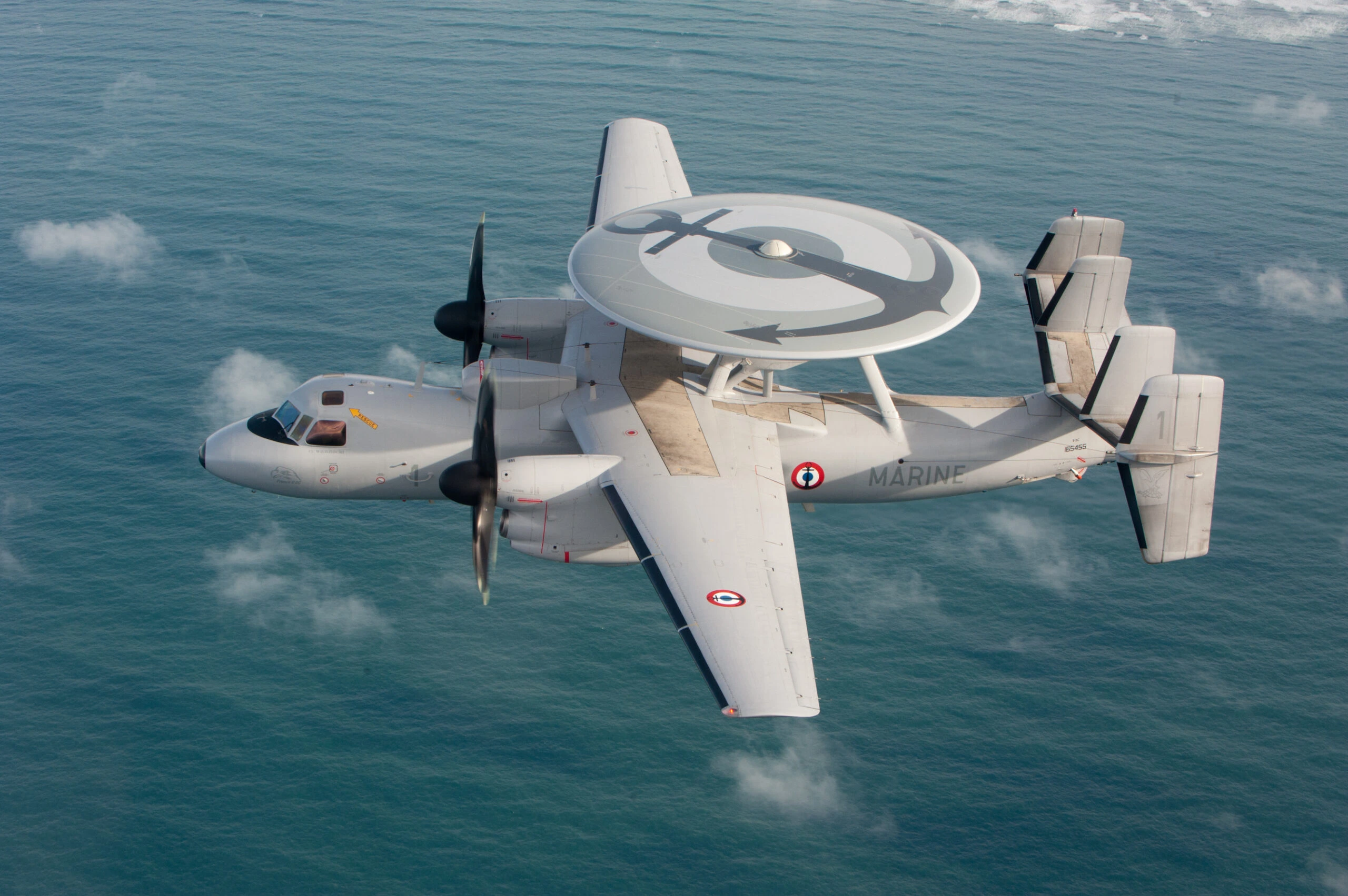 Un E-2 Hawkeye de la Marine nationale en vol au-dessus de la mer, radar rotodome sur le dos